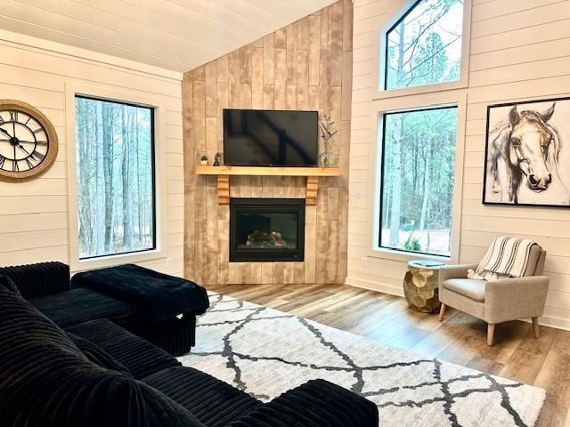 living room with vaulted ceiling, wooden walls, a fireplace, and light hardwood / wood-style flooring