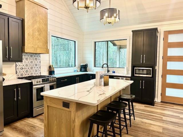 kitchen with hanging light fixtures, stainless steel appliances, light stone countertops, a kitchen island, and vaulted ceiling