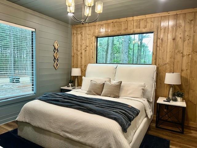 bedroom with multiple windows, a notable chandelier, hardwood / wood-style floors, and wood walls