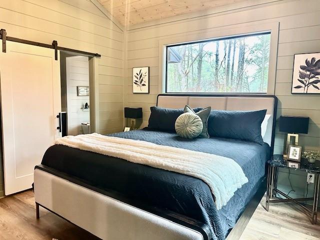 bedroom with hardwood / wood-style flooring, a barn door, lofted ceiling, and wooden walls