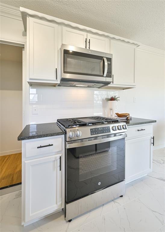 kitchen featuring white cabinetry, decorative backsplash, stainless steel appliances, and dark stone countertops