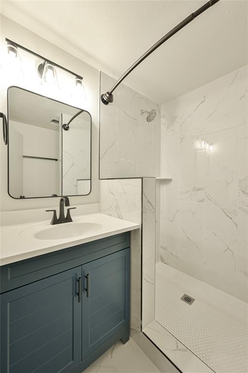 bathroom with tiled shower and vanity