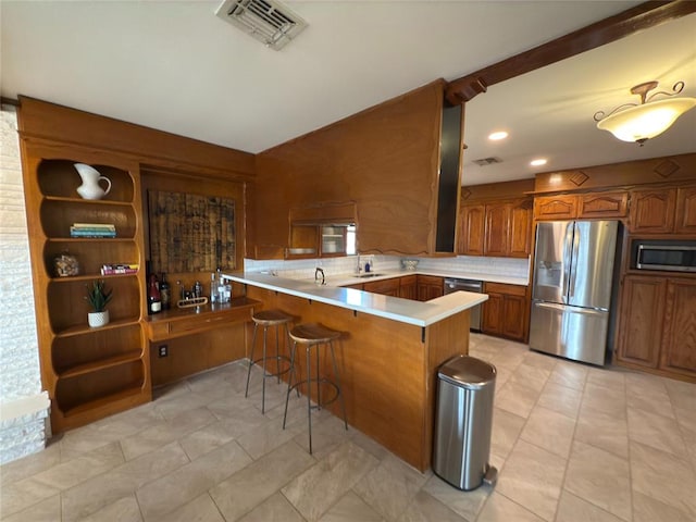 kitchen featuring sink, appliances with stainless steel finishes, backsplash, a kitchen bar, and kitchen peninsula