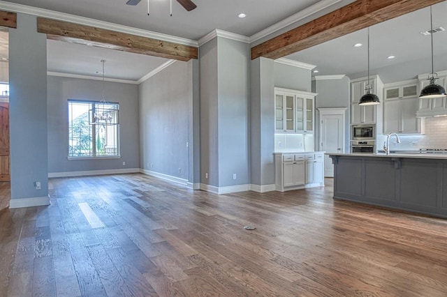 unfurnished living room featuring ornamental molding, ceiling fan with notable chandelier, sink, and hardwood / wood-style floors