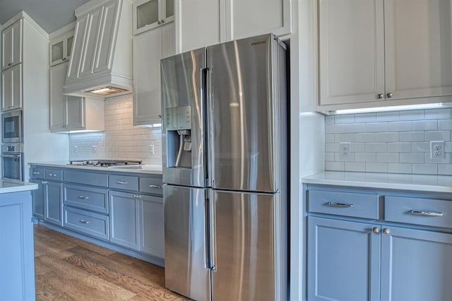 kitchen featuring dark wood-type flooring, backsplash, appliances with stainless steel finishes, custom range hood, and white cabinets