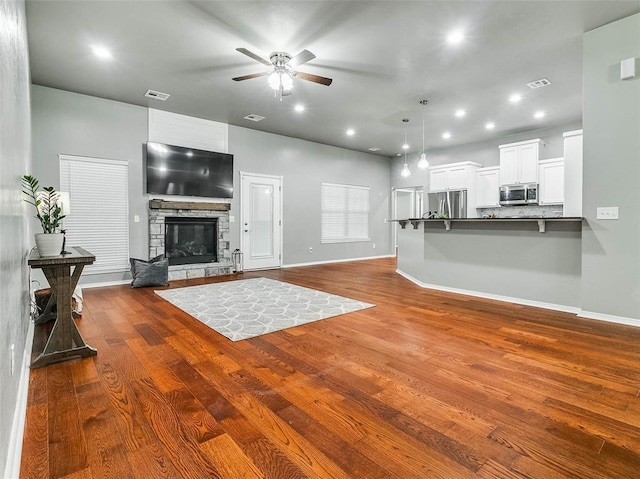 living room featuring hardwood / wood-style flooring, ceiling fan, and a stone fireplace