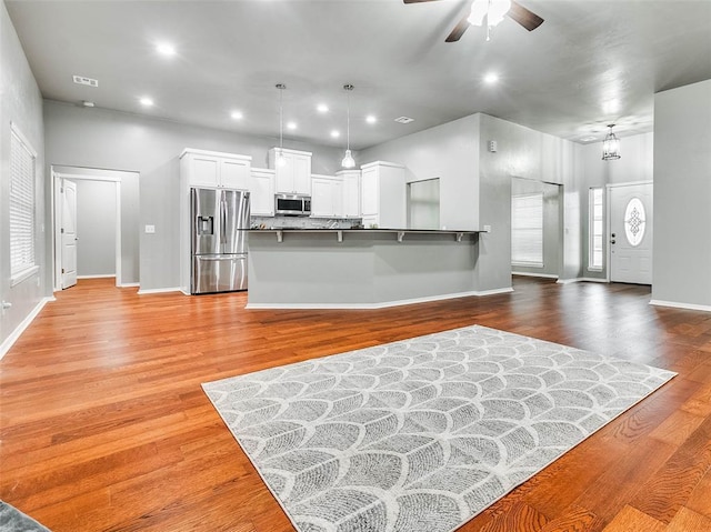 kitchen with decorative light fixtures, kitchen peninsula, stainless steel appliances, light hardwood / wood-style floors, and white cabinets