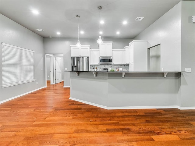 kitchen featuring white cabinetry, stainless steel appliances, kitchen peninsula, and a kitchen bar