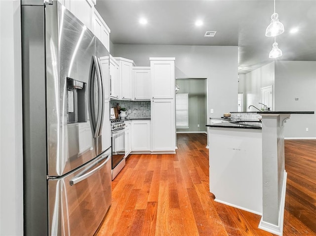 kitchen featuring stainless steel appliances, hanging light fixtures, white cabinets, and light hardwood / wood-style flooring