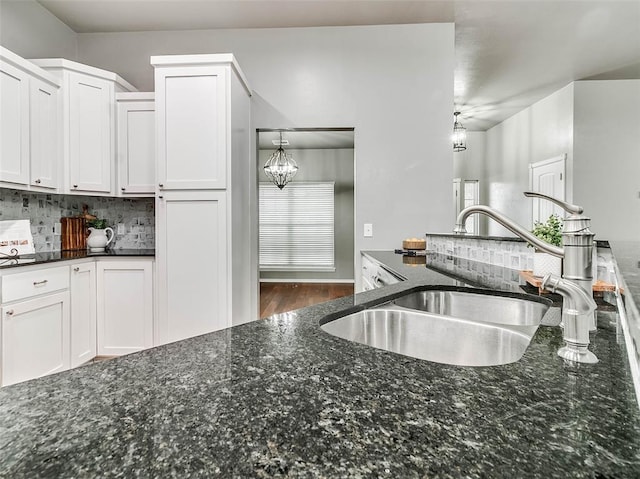 kitchen with white cabinetry, hanging light fixtures, sink, and dark stone counters