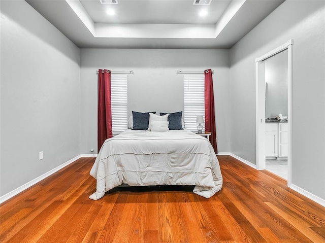 bedroom with hardwood / wood-style floors, ensuite bath, and a tray ceiling