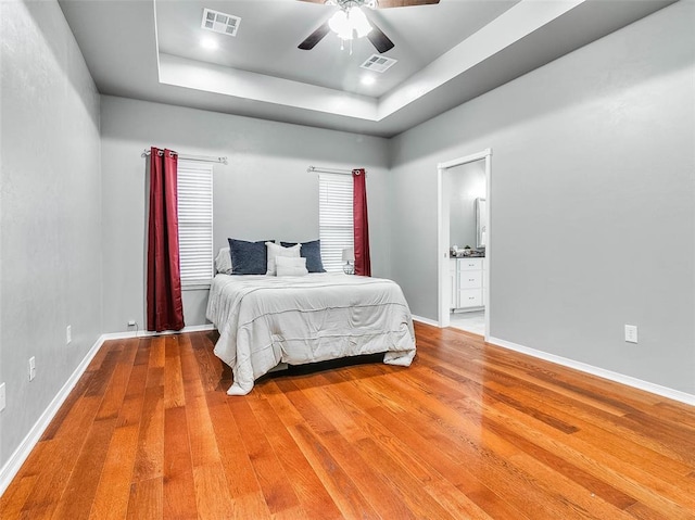 bedroom featuring ceiling fan, ensuite bathroom, a tray ceiling, and hardwood / wood-style floors