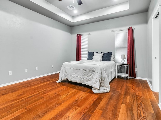 bedroom with hardwood / wood-style flooring, ceiling fan, and a tray ceiling