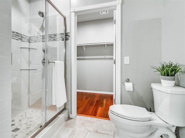 bathroom featuring hardwood / wood-style floors, a shower with door, and toilet