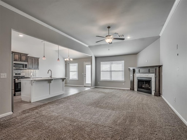 unfurnished living room with lofted ceiling, a high end fireplace, ornamental molding, light carpet, and ceiling fan with notable chandelier