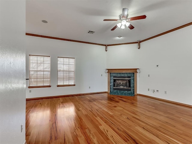 unfurnished living room featuring a tiled fireplace, ornamental molding, ceiling fan, and light wood-type flooring