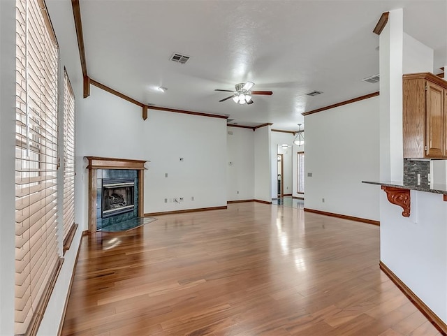 unfurnished living room featuring a tiled fireplace, ornamental molding, light hardwood / wood-style floors, and ceiling fan