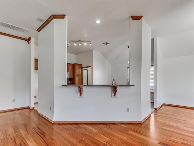 kitchen featuring track lighting, light hardwood / wood-style floors, vaulted ceiling, kitchen peninsula, and dark stone counters