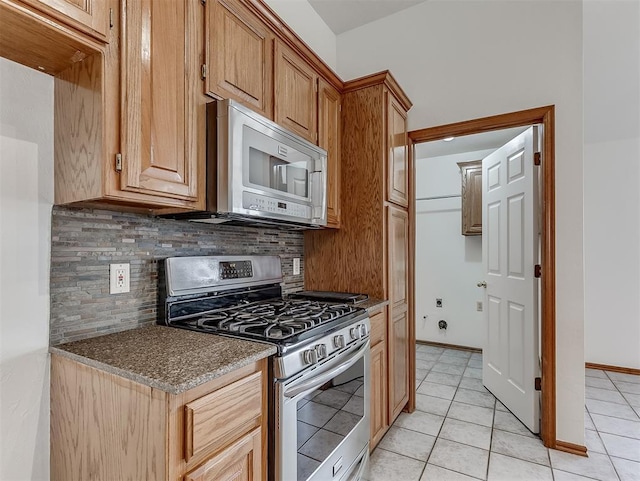 kitchen featuring tasteful backsplash, light tile patterned flooring, dark stone countertops, and appliances with stainless steel finishes