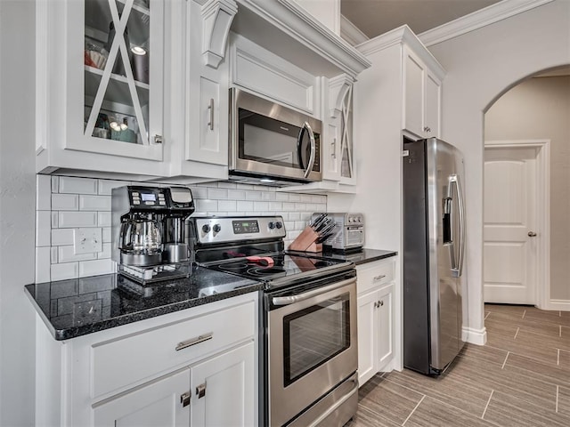 kitchen featuring white cabinetry, stainless steel appliances, tasteful backsplash, and dark stone countertops