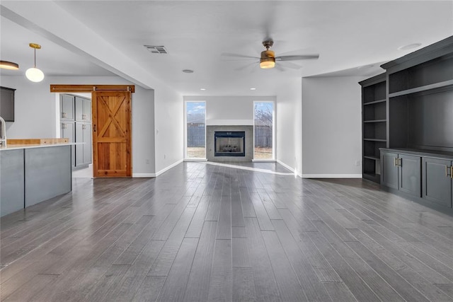 unfurnished living room with dark wood-type flooring, a barn door, and ceiling fan