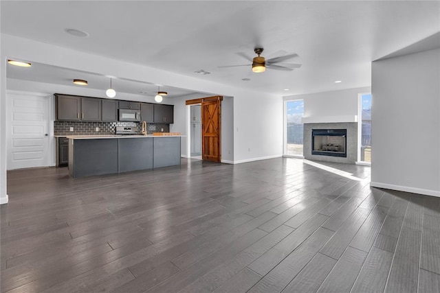 unfurnished living room featuring dark wood-type flooring, ceiling fan, and a barn door