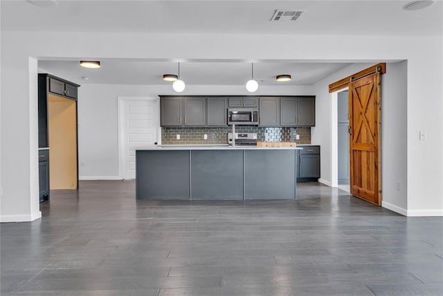 kitchen featuring gray cabinets, appliances with stainless steel finishes, backsplash, decorative light fixtures, and a barn door