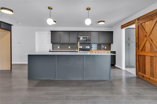 kitchen featuring pendant lighting, a center island with sink, a barn door, and appliances with stainless steel finishes