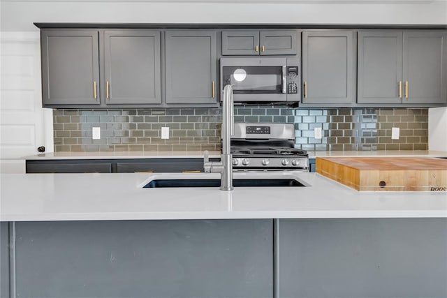 kitchen with tasteful backsplash, appliances with stainless steel finishes, gray cabinets, and sink