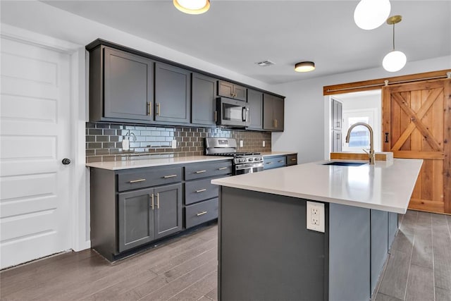 kitchen with sink, hanging light fixtures, a center island with sink, stainless steel appliances, and a barn door