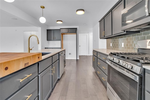 kitchen with appliances with stainless steel finishes, wood-type flooring, gray cabinetry, decorative backsplash, and hanging light fixtures