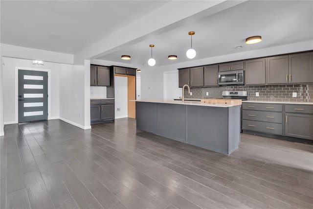 kitchen featuring sink, tasteful backsplash, decorative light fixtures, a center island with sink, and appliances with stainless steel finishes