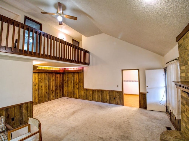 living room with high vaulted ceiling, a textured ceiling, wooden walls, carpet floors, and ceiling fan