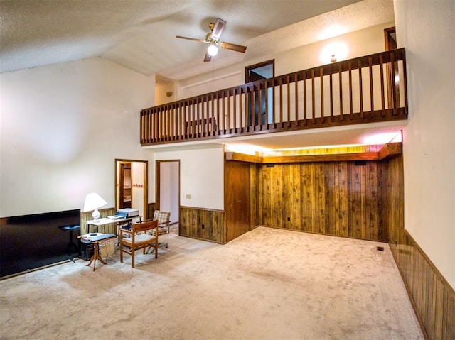 living room with a textured ceiling, light colored carpet, ceiling fan, and wood walls