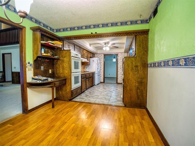 kitchen with white appliances, ceiling fan, light hardwood / wood-style floors, a raised ceiling, and a textured ceiling