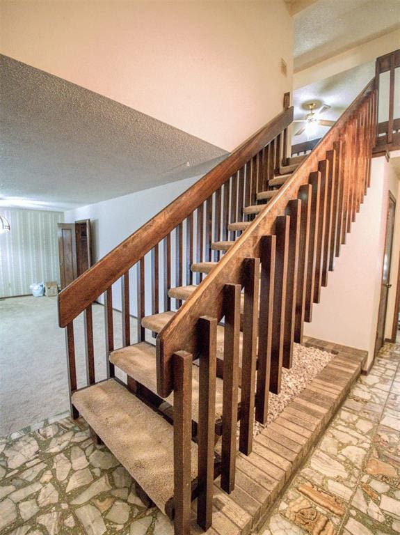 stairs featuring ceiling fan, carpet, and a textured ceiling