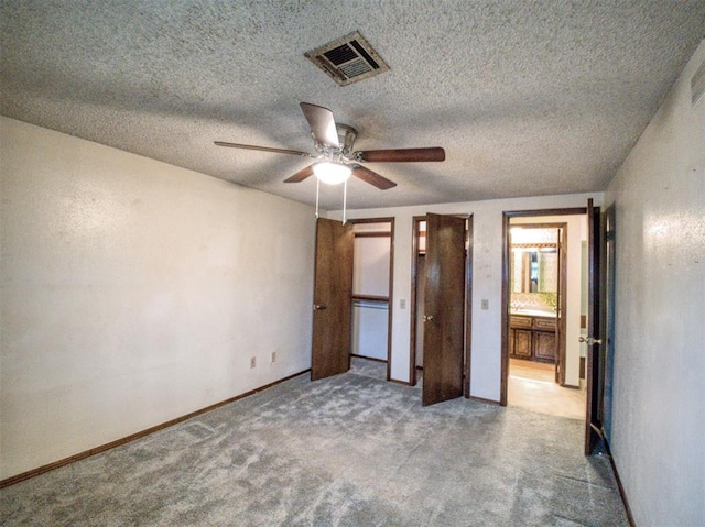 unfurnished bedroom with ceiling fan, connected bathroom, light carpet, and a textured ceiling