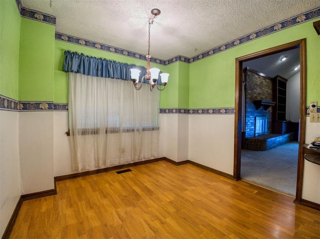 7318 Hummingbird Cir, Oklahoma City, OK 73162 - unfurnished room featuring a chandelier, wood finished floors, a textured ceiling, and a fireplace