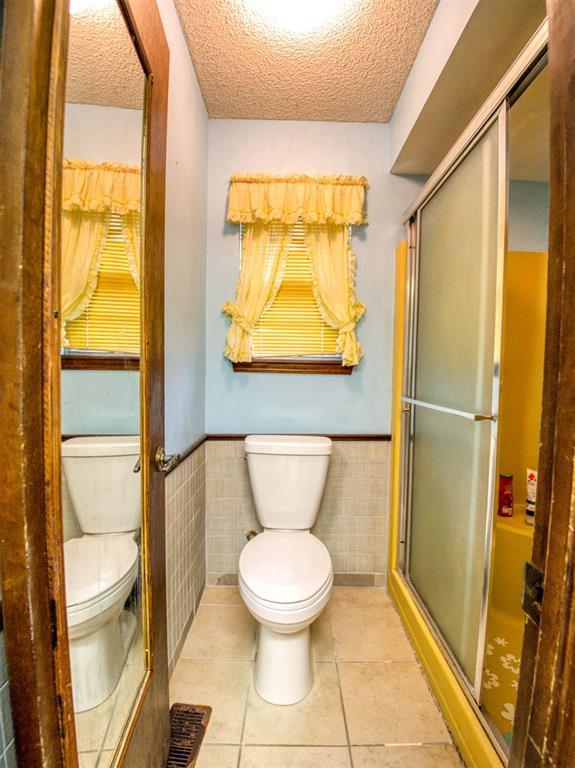7318 Hummingbird Cir, Oklahoma City, OK 73162 - bathroom featuring wainscoting, tile walls, a textured ceiling, a shower stall, and tile patterned floors
