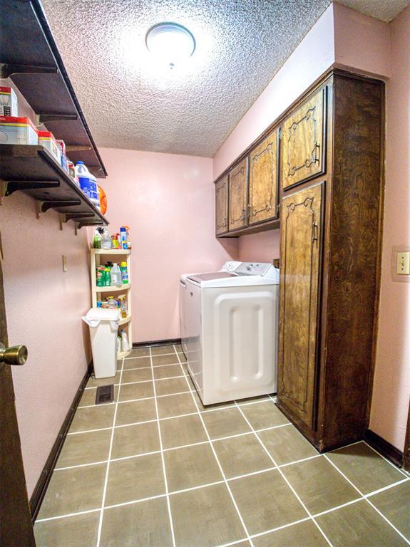 7318 Hummingbird Cir, Oklahoma City, OK 73162 - laundry room featuring a textured ceiling, washer and clothes dryer, tile patterned floors, and cabinet space