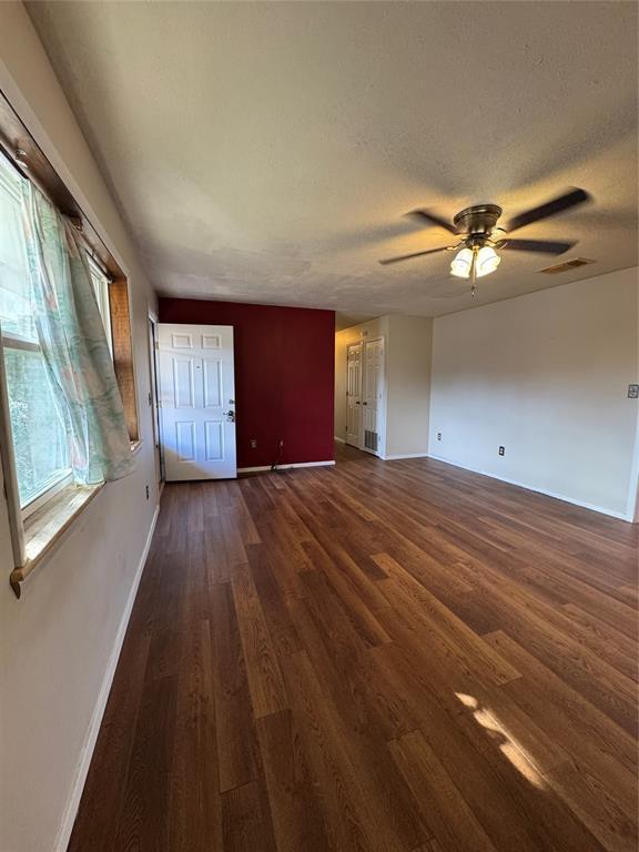 unfurnished living room with ceiling fan, dark wood-type flooring, and a textured ceiling