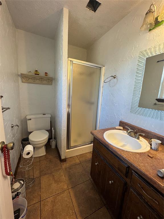 bathroom with vanity, toilet, a shower with door, tile patterned floors, and a textured ceiling