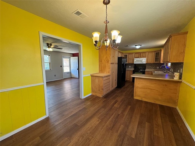 kitchen featuring decorative light fixtures, dark hardwood / wood-style flooring, black refrigerator, kitchen peninsula, and range