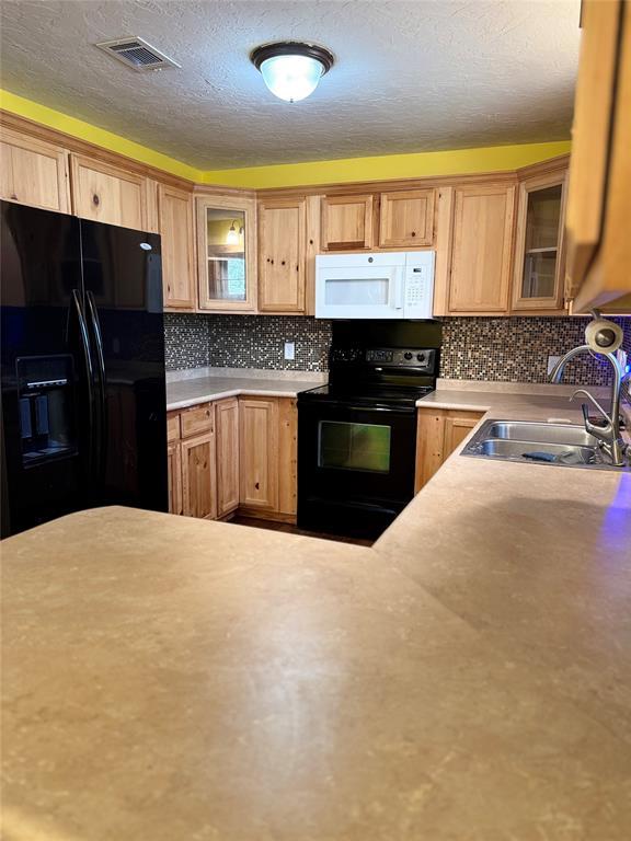 kitchen with sink, a textured ceiling, black appliances, and backsplash