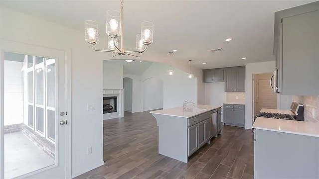 kitchen featuring pendant lighting, stainless steel appliances, a notable chandelier, an island with sink, and dark hardwood / wood-style flooring