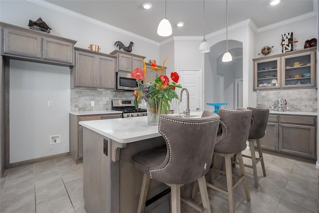 kitchen with crown molding, a breakfast bar, a kitchen island with sink, hanging light fixtures, and stainless steel appliances