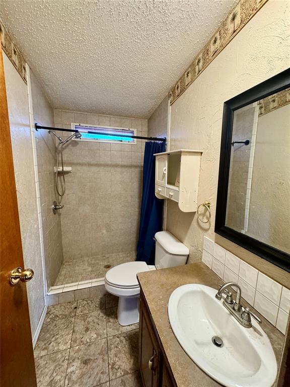 bathroom with vanity, toilet, a textured ceiling, and walk in shower