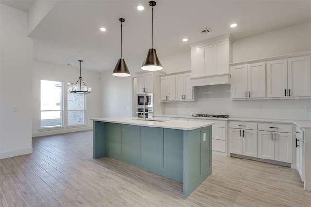 kitchen with pendant lighting, stainless steel microwave, white cabinetry, and a kitchen island with sink