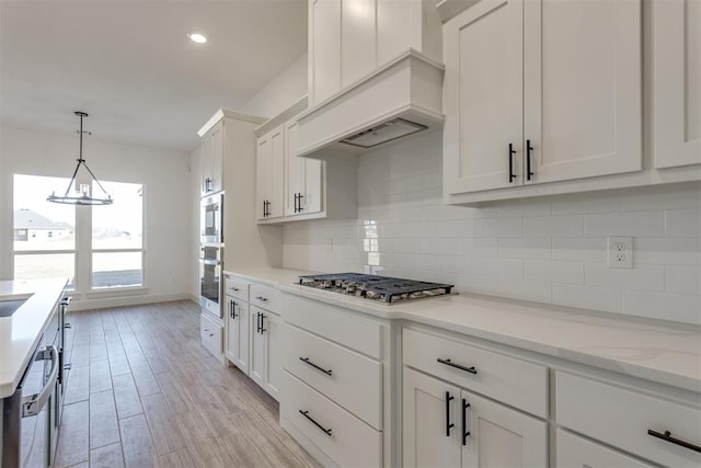 kitchen with white cabinetry, stainless steel appliances, decorative backsplash, decorative light fixtures, and light wood-type flooring