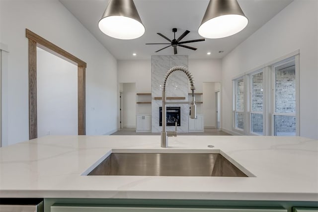 kitchen featuring a fireplace, green cabinetry, sink, ceiling fan, and light stone counters